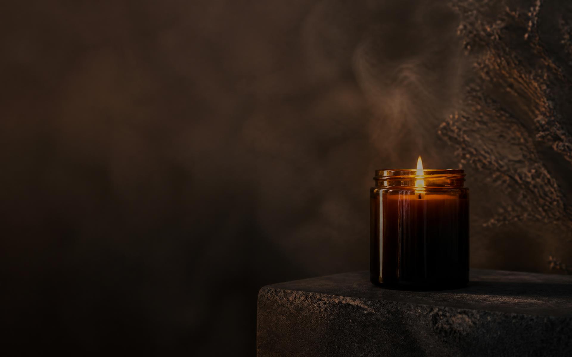 A lit NOCTÉ candle glowing on a dark stone ledge with drifting smoke